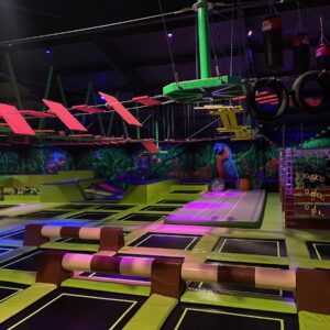 Hala trampolin Jungle Park Pruszków w neonowym świetle, nad nią park linowy